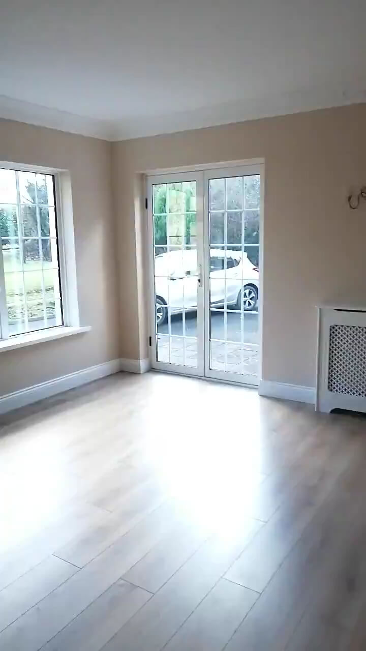  porition of a living room with white framed french doors and window, light brown laminate flooring, magnolia walls and a white radiator cover